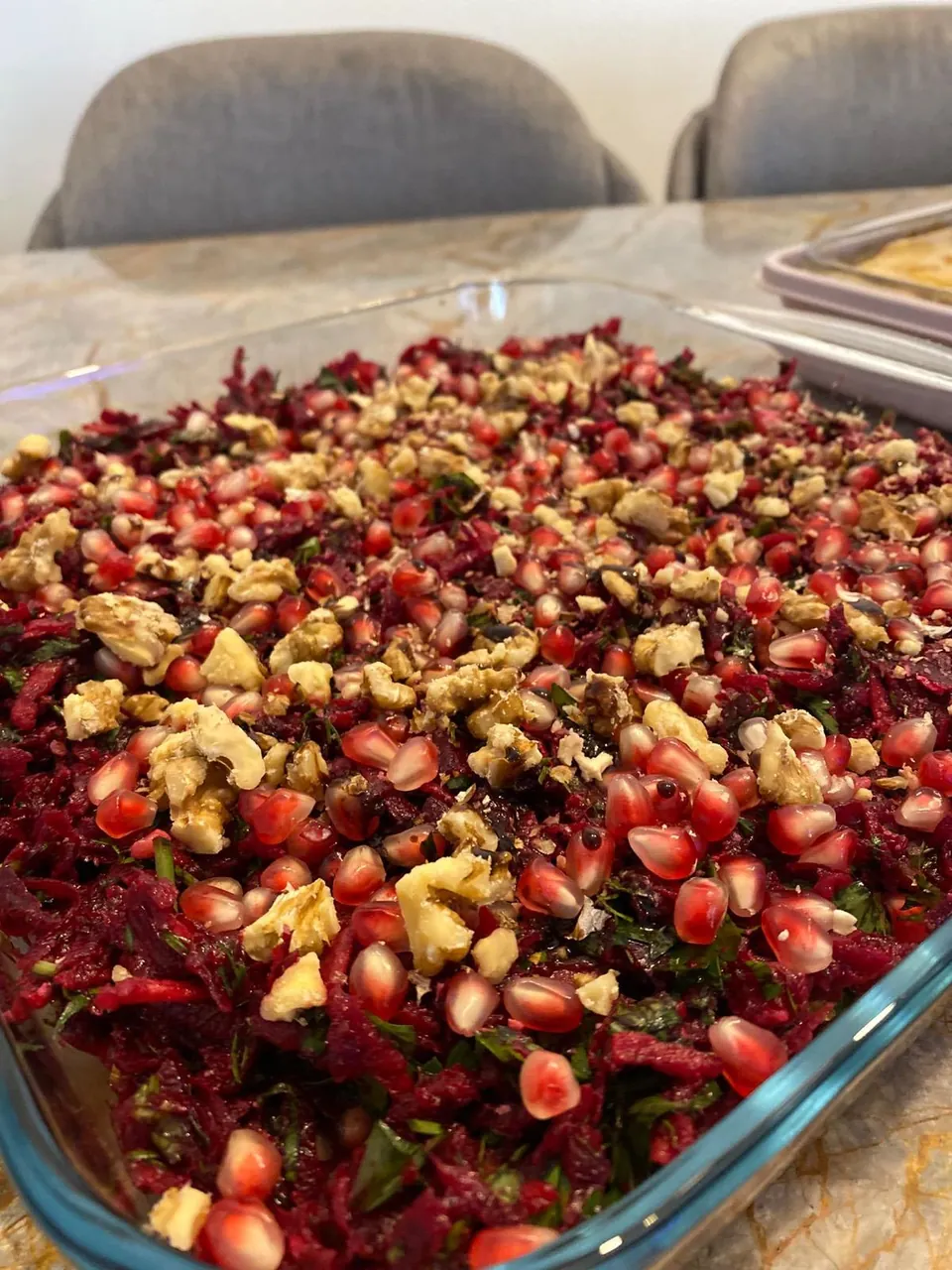 Cam fırın kabında rendelenmiş pancar salatası, üzerinde nar taneleri ve ceviz parçaları